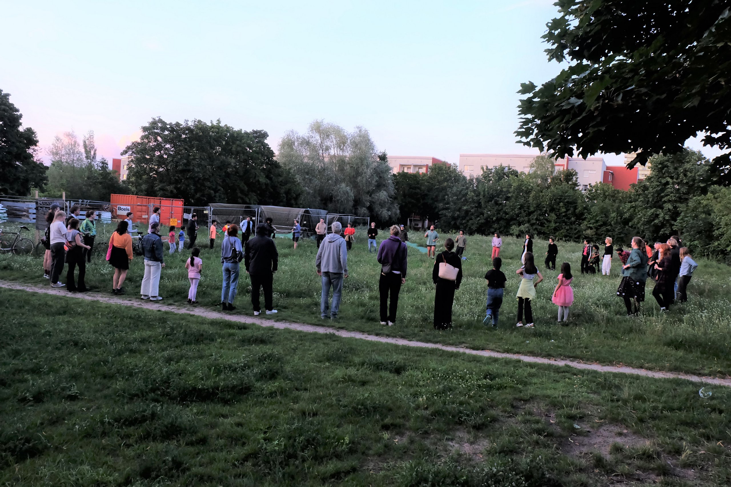 Eine große Menschengruppe steht in einem grünen Park im Kreis.