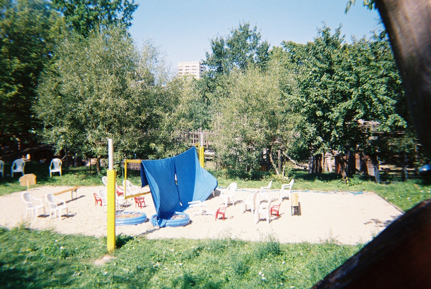 Ein Beachvolleyballfeld in einem Park. Im Hin tergrund sind Bäume und dann ein Hochhaus zu erkennen. Die Felder sind mit mit Stühlen in den Spielflächen bestückt. In der Mitte auf dem netz hängen zwei große dunkle Laken.