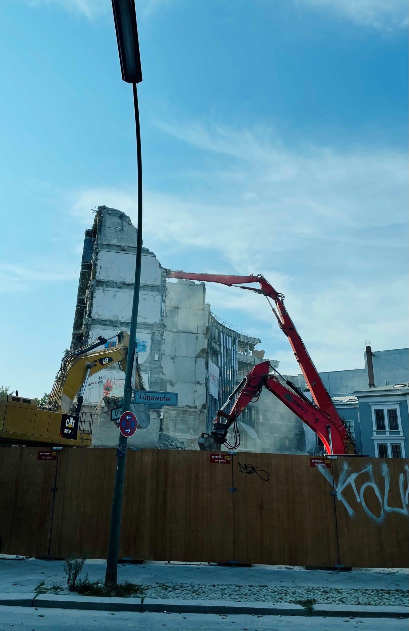Hinter einem Holz-Bauzaun in der Lützowstraße stehen zwei Bagger auf einer Baustelle. Dahinter ist eine abgerissene Hauswand, die noch zur Hälfte steht.