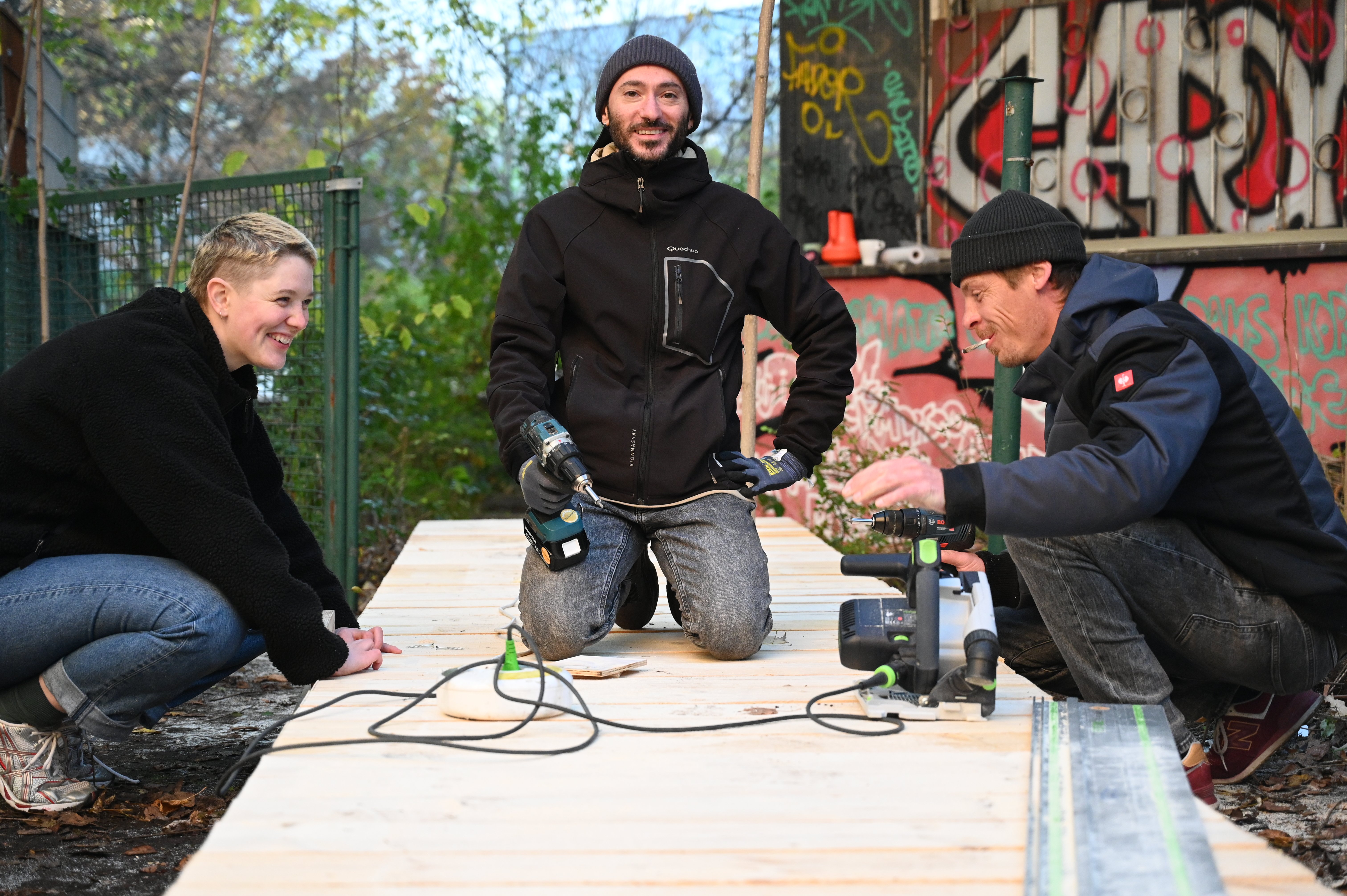 Drei Personen bauen an einer Holzfläche mit Maschinen.