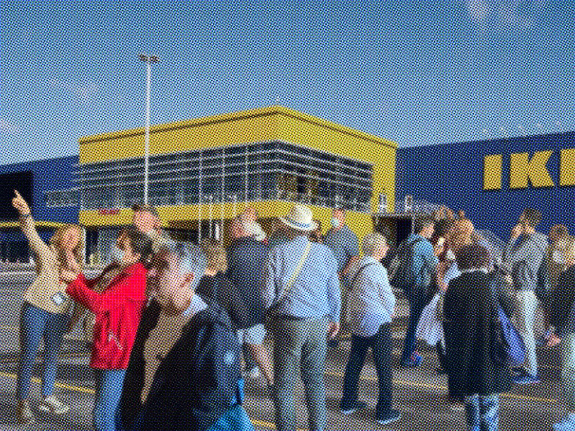 Siebzehn Männer und Frauen stehen vor einer Ikea Filiale und schauen in unterschiedliche Richtungen. Zwei Personen zeigen in den Himmel.