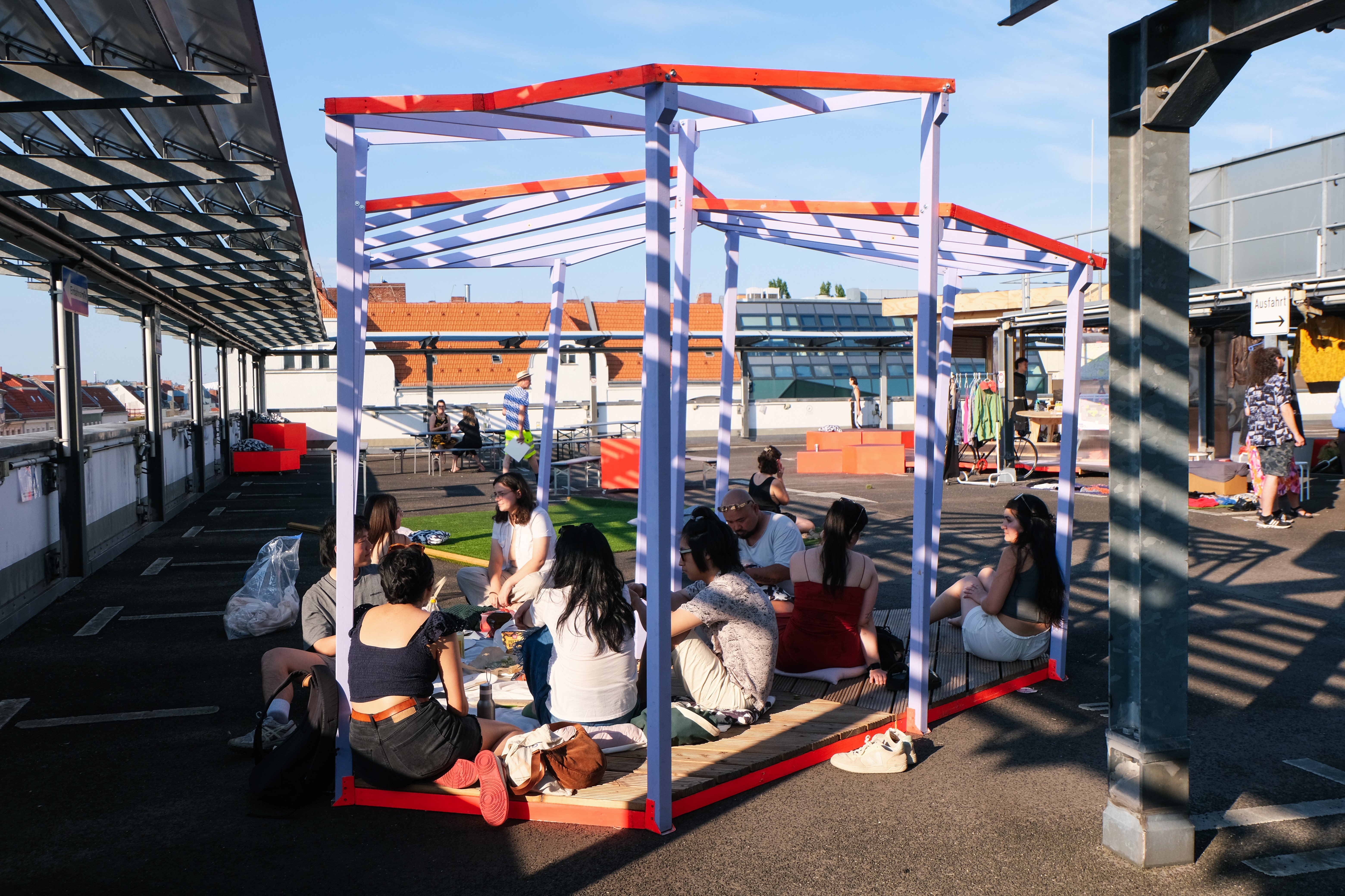 Das Bild zeigt eine lebendige Szene auf einem Parkdeck. Menschen unterschiedlichen Alters sind in Gruppen versammelt, unterhalten sich und genießen die entspannte Atmosphäre.
