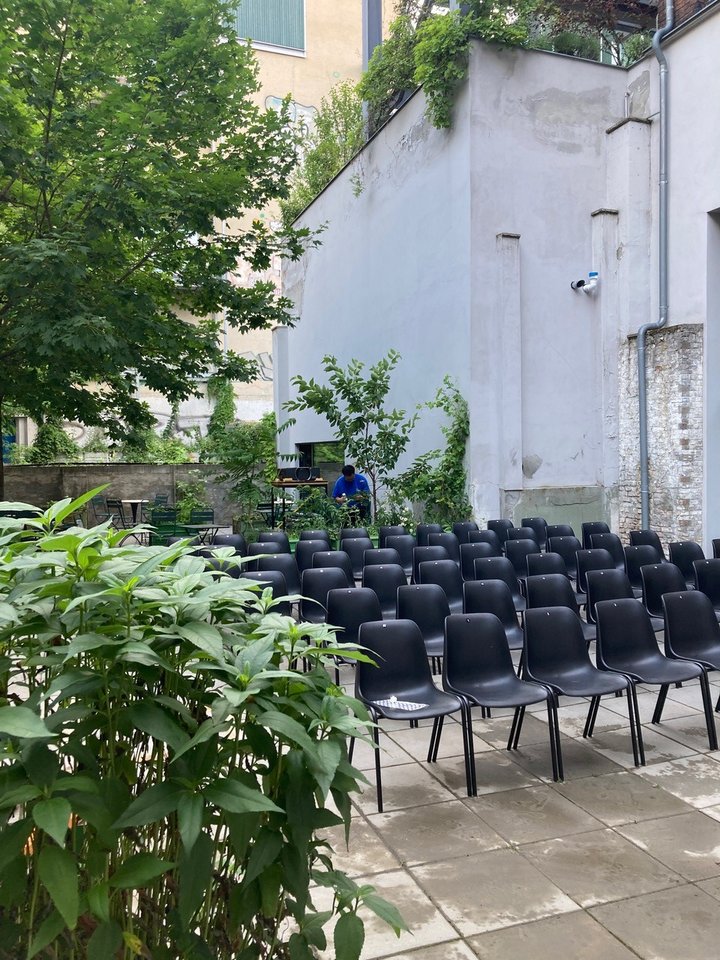 Ein Foto der Außenfläche des Kinos. Es sind Stuhlreihen aufgestellt und es stehen viele Pflanzen um diese Stühle.
