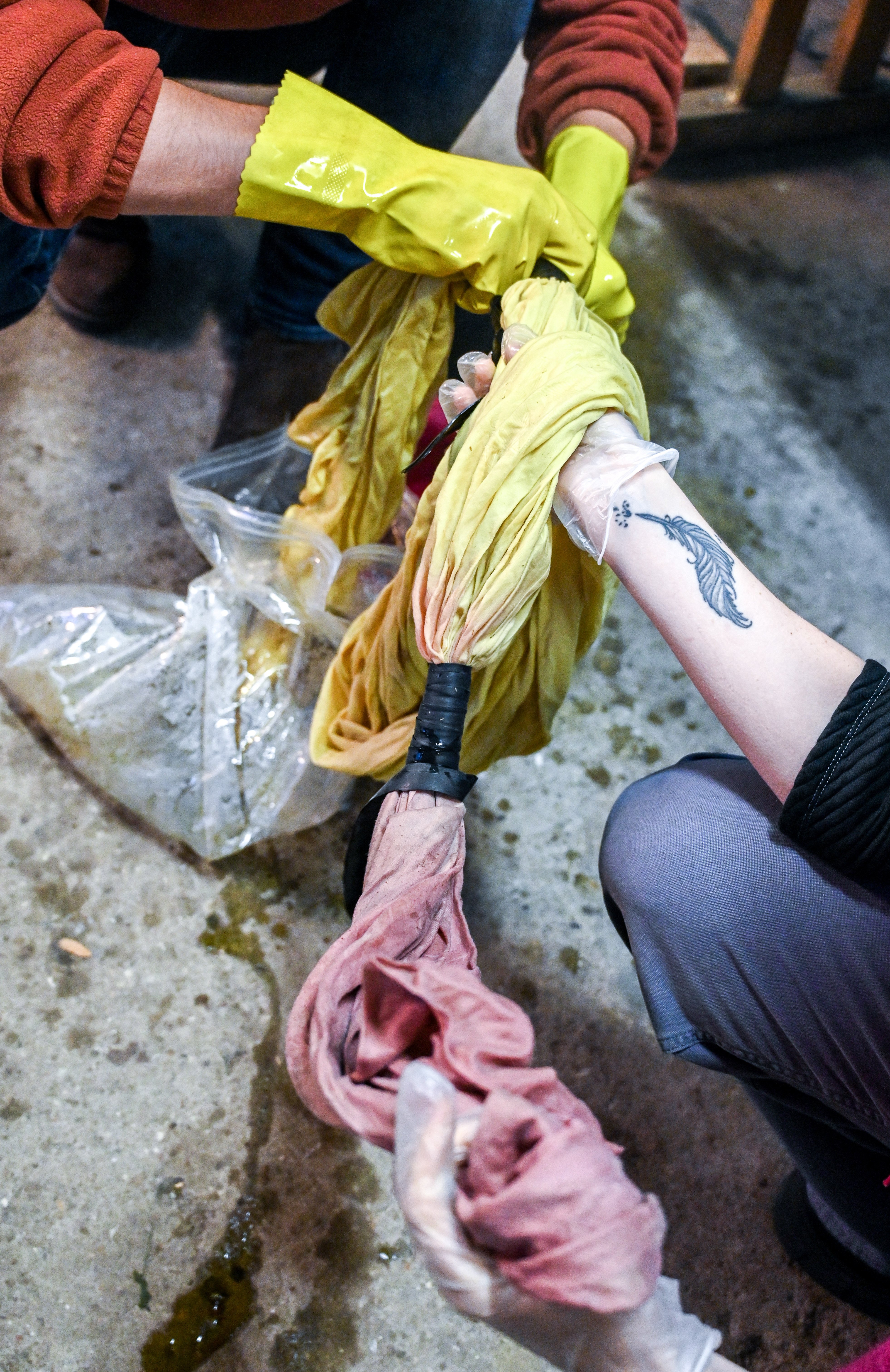 Zwei Personen halten einen gefärbten Stoff mit Handschuhen.