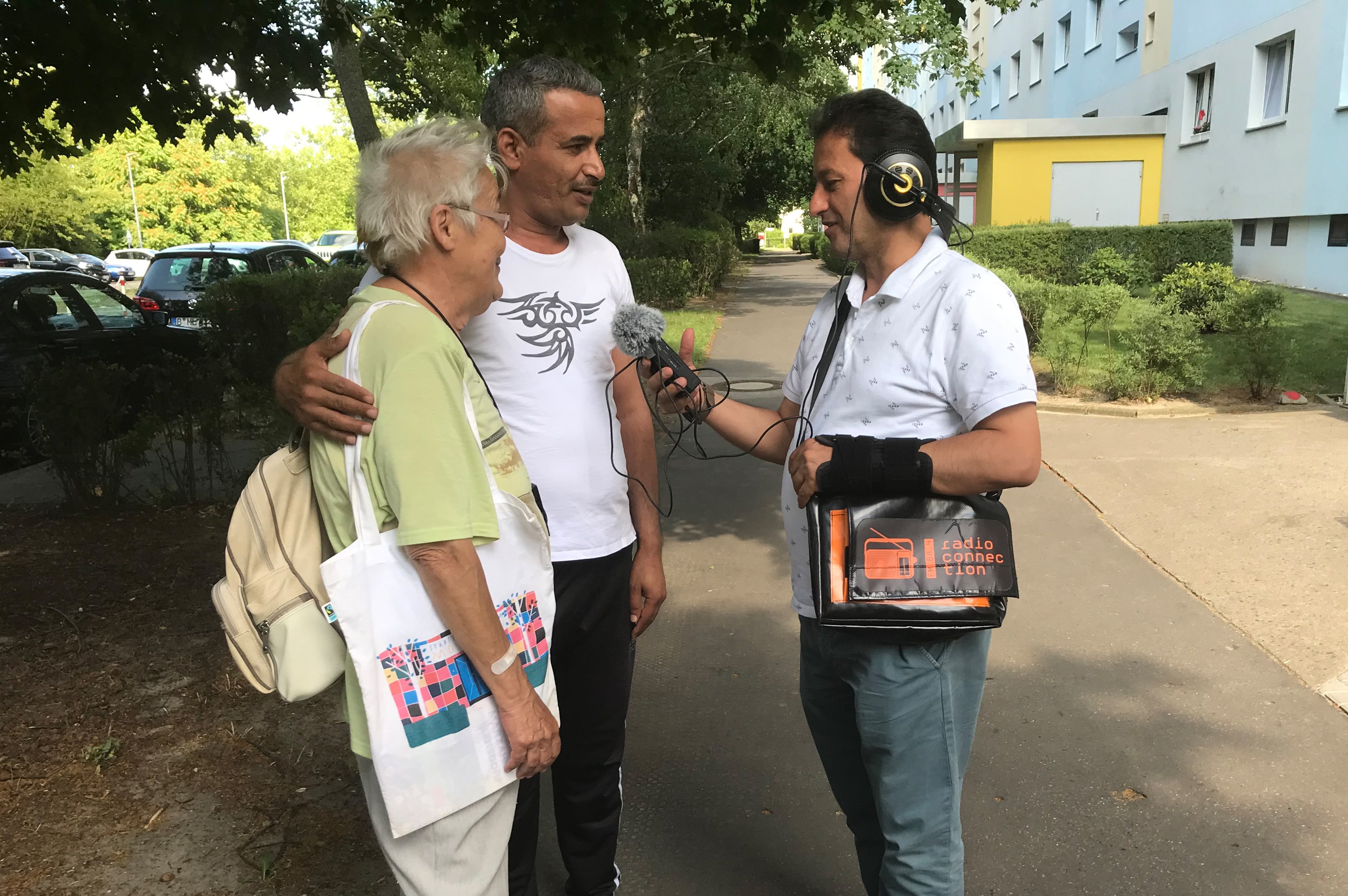 Ein Mann mit Kopfhörer und Mikrofon interviewt eine ältere Frau und einen Mann