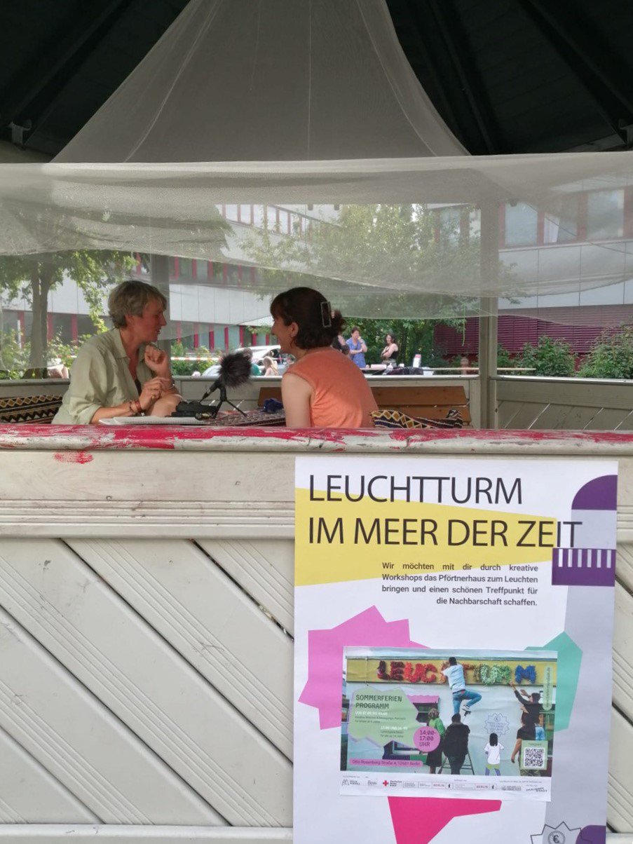 Ein Foto von zwei Personen, die den Podcast “Zeit fragen“ aufnehmen. Sie sitzen in einem Pavillon an einem Tisch, zwischen ihnen steht ein Mikrophon.